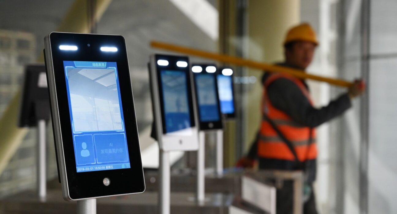 A construction worker walks past facial recognition screens at the entrance to the terminal building of the new Beijing Daxing International Airport, in Beijing on March 1, 2019. (Photo: Greg Baker/AFP)