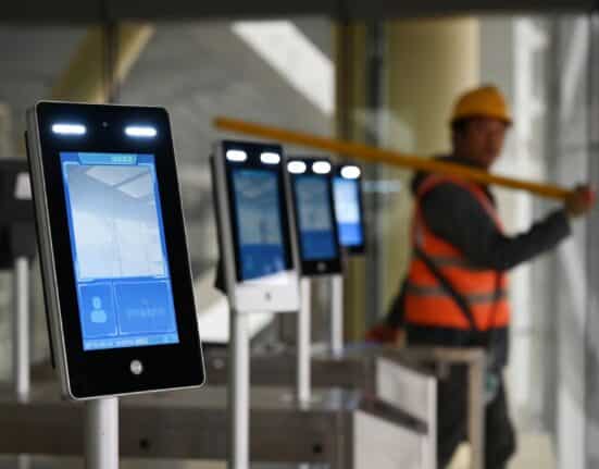 A construction worker walks past facial recognition screens at the entrance to the terminal building of the new Beijing Daxing International Airport, in Beijing on March 1, 2019. (Photo: Greg Baker/AFP)