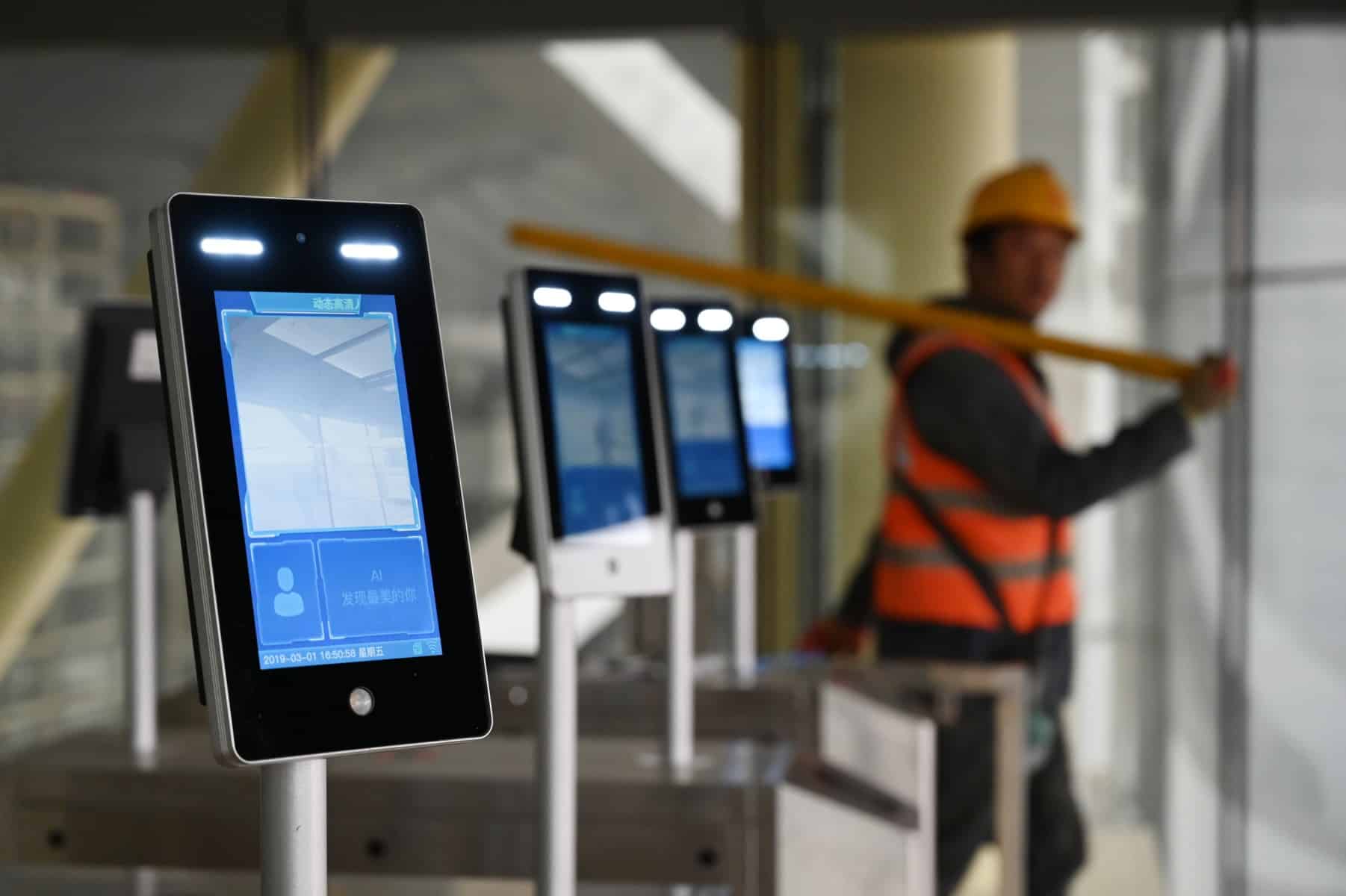 A construction worker walks past facial recognition screens at the entrance to the terminal building of the new Beijing Daxing International Airport, in Beijing on March 1, 2019. (Photo: Greg Baker/AFP)