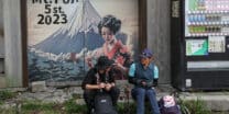 This photo taken on August 31, 2023 shows two visitors resting at the fifth stage on the slopes of Mount Fuji, Japan's highest peak at 3,776 metres (12,388 feet). With its millions of visitors every year and the buses, supply trucks, noodle shops and fridge magnets, Mount Fuji is no longer the peaceful, nature-filled pilgrimage site it once was. (Photo by Mathias Cena / AFP)