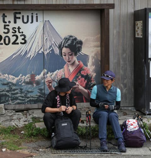 This photo taken on August 31, 2023 shows two visitors resting at the fifth stage on the slopes of Mount Fuji, Japan's highest peak at 3,776 metres (12,388 feet). With its millions of visitors every year and the buses, supply trucks, noodle shops and fridge magnets, Mount Fuji is no longer the peaceful, nature-filled pilgrimage site it once was. (Photo by Mathias Cena / AFP)