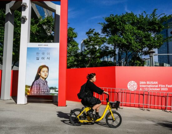 A woman cycles past a poster of South Korean actress Go Ah-sung for the film 'Because I Hate Korea' at the Busan Cinema Center before the opening of the 28th Busan International Film Festival (BIFF) in Busan on October 4, 2023. (Photo by Anthony Wallace/ AFP)