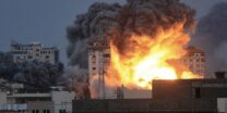 People standing on a rooftop watch as a ball of fire and smoke rises above a building in Gaza City on October 7, 2023 during an Israeli air strike that hit the Palestine Tower building. (Photo by Mahmud Hams / AFP)