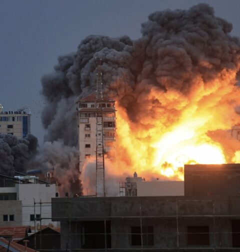 People standing on a rooftop watch as a ball of fire and smoke rises above a building in Gaza City on October 7, 2023 during an Israeli air strike that hit the Palestine Tower building. (Photo by Mahmud Hams / AFP)